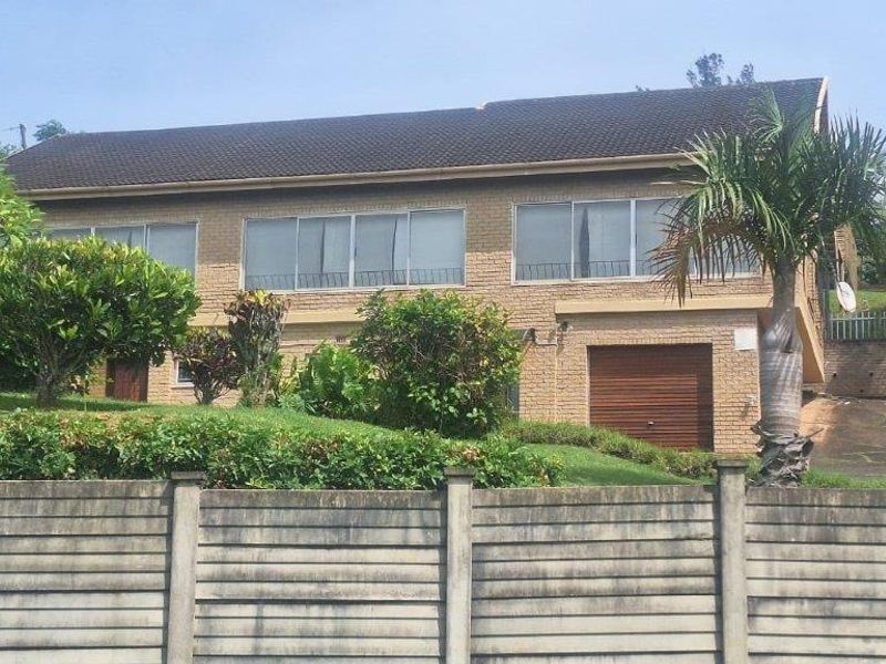 A two-story brick residential house featuring a tiled roof, integrated garage, and a concrete boundary wall with a landscaped front garden.