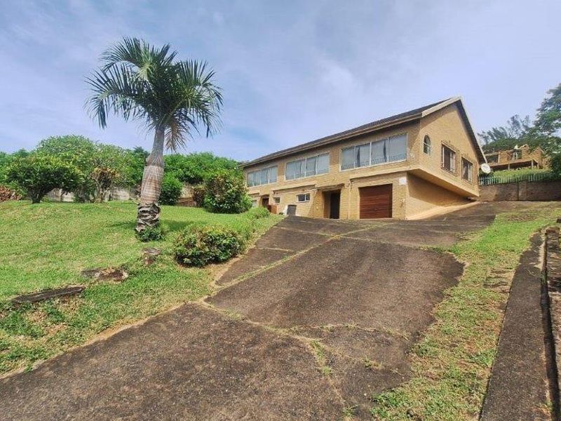 Front exterior view of a brick house featuring a concrete driveway, garage access, and established garden surroundings.