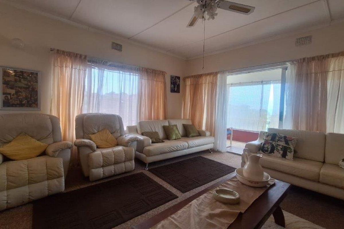 A spacious living room featuring carpeted flooring, a ceiling fan, and large windows with sliding door access to an outdoor area.