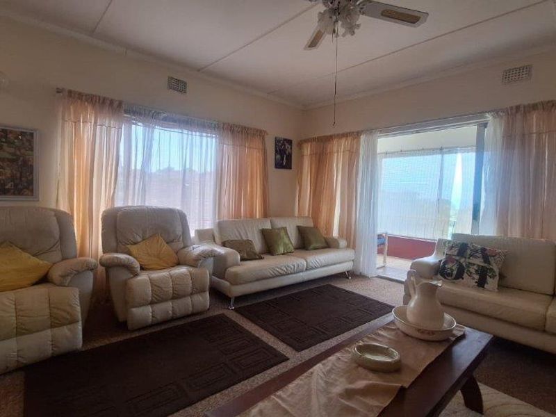 A spacious living room featuring carpeted flooring, a ceiling fan, and large windows with sliding door access to an outdoor area.