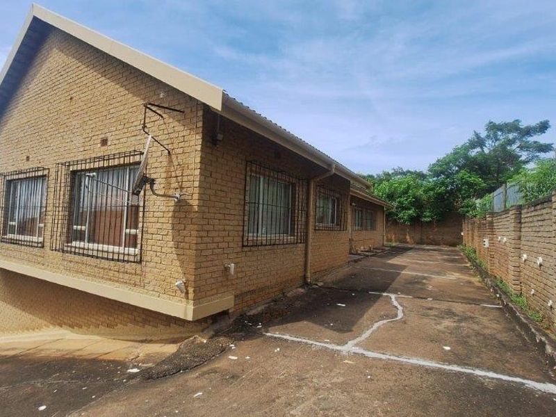 Rear exterior view of a face brick house featuring a concrete driveway, security bars on windows, and a perimeter retaining wall.