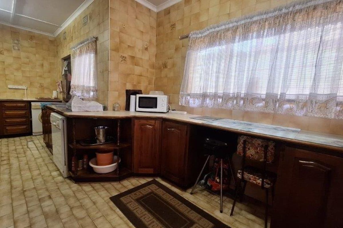 A dated kitchen featuring extensive wall tiling, wooden cabinetry, and laminate countertops, offering significant potential for a modern renovation.