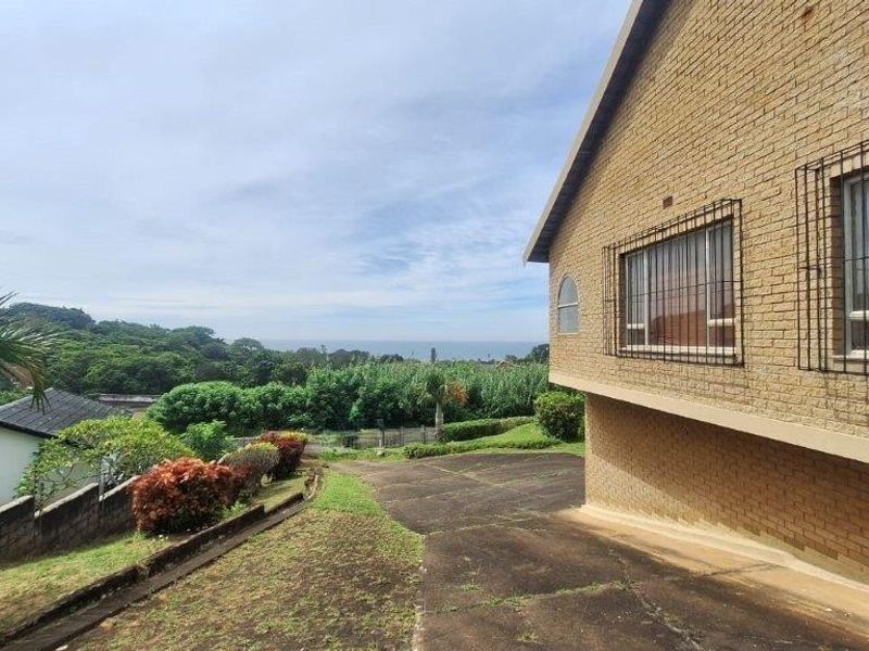 Rear view of the property featuring a face brick facade, security bars on windows, and a concrete driveway overlooking a scenic landscape.