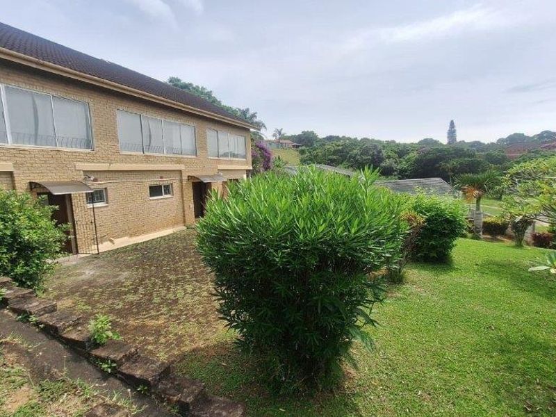Rear view of a double-story brick house featuring large sliding windows and a spacious garden with a stone retaining wall.
