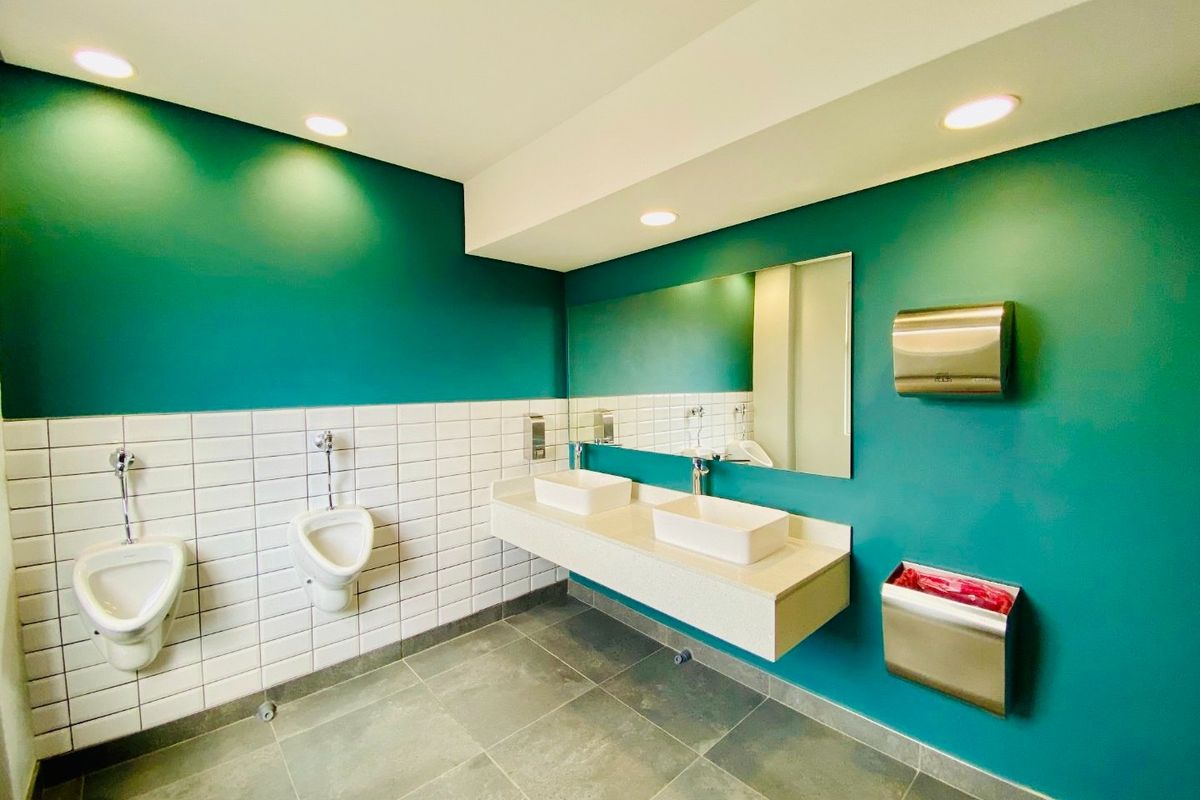 Modern commercial restroom featuring dual vessel sinks on a floating vanity, wall-mounted urinals, and contemporary teal wall finishes with clean white tiling.