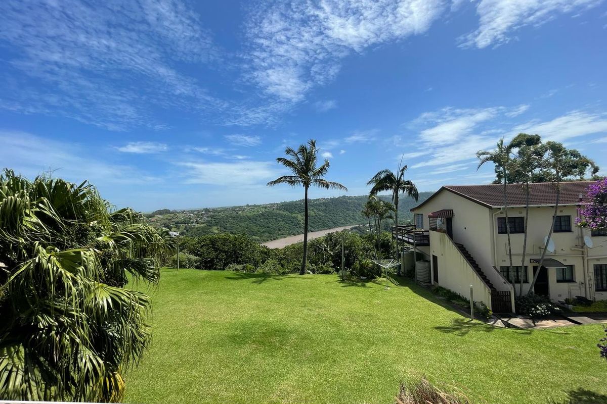 A spacious rear garden with a well-maintained lawn, overlooking a scenic river valley and surrounding landscape, featuring an elevated balcony and external staircase.