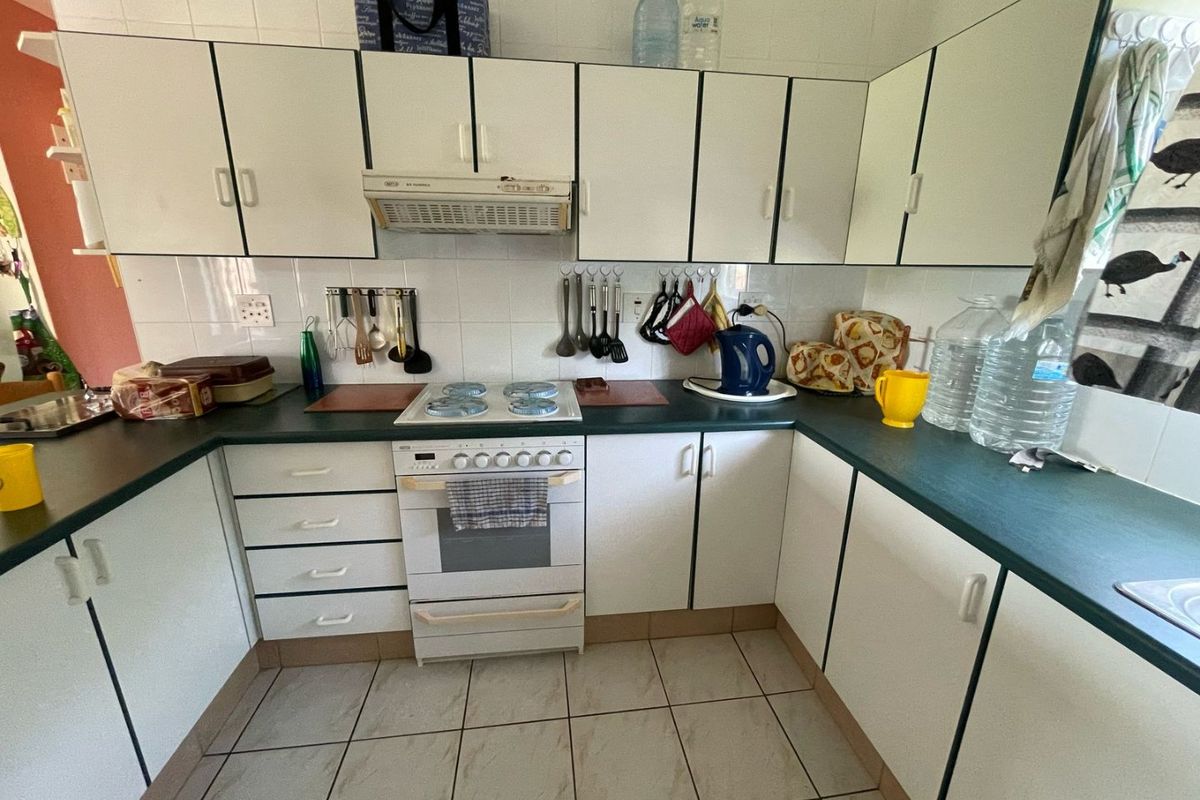 A functional kitchen featuring white cabinetry, dark laminate countertops, ceramic tile flooring, and a built-in extractor fan above a freestanding stove.
