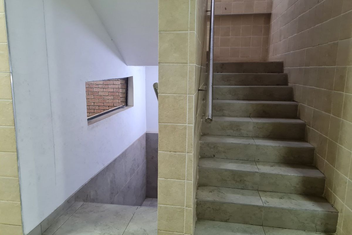 A functional stairwell featuring tiled steps, a stainless steel handrail, and ceramic wall tiling in a neutral color palette.