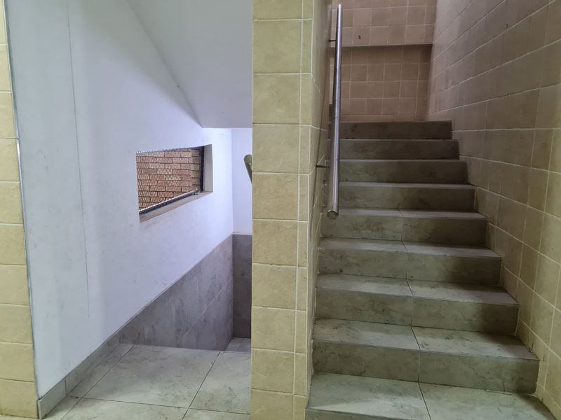 A functional stairwell featuring tiled steps, a stainless steel handrail, and ceramic wall tiling in a neutral color palette.