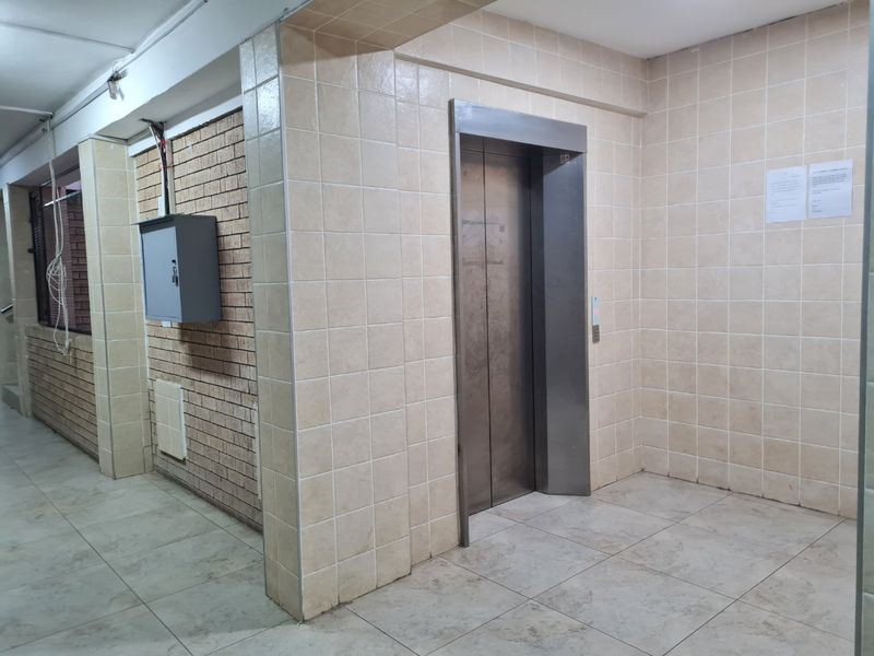 A communal apartment hallway featuring a metal elevator, tiled walls and flooring, and exposed brick accents.
