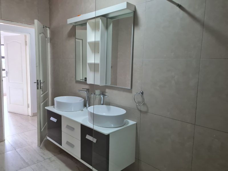 Modern bathroom featuring a double vanity with vessel sinks, a wall-mounted mirror cabinet, and neutral floor-to-ceiling wall tiles.