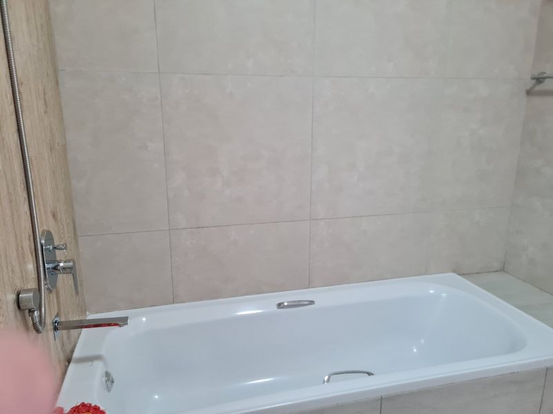 A clean bathroom featuring a built-in bathtub with modern chrome fixtures and neutral ceramic wall tiling.