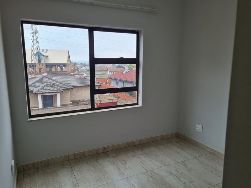 An empty bedroom featuring neutral tiled flooring, a large aluminium-framed window, and clean wall finishes, offering a bright and versatile living space.