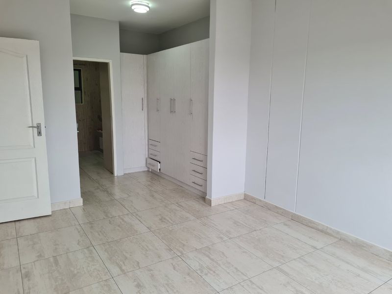 A bright, empty bedroom featuring neutral tiled flooring and extensive built-in cupboard storage with a clean, modern finish.