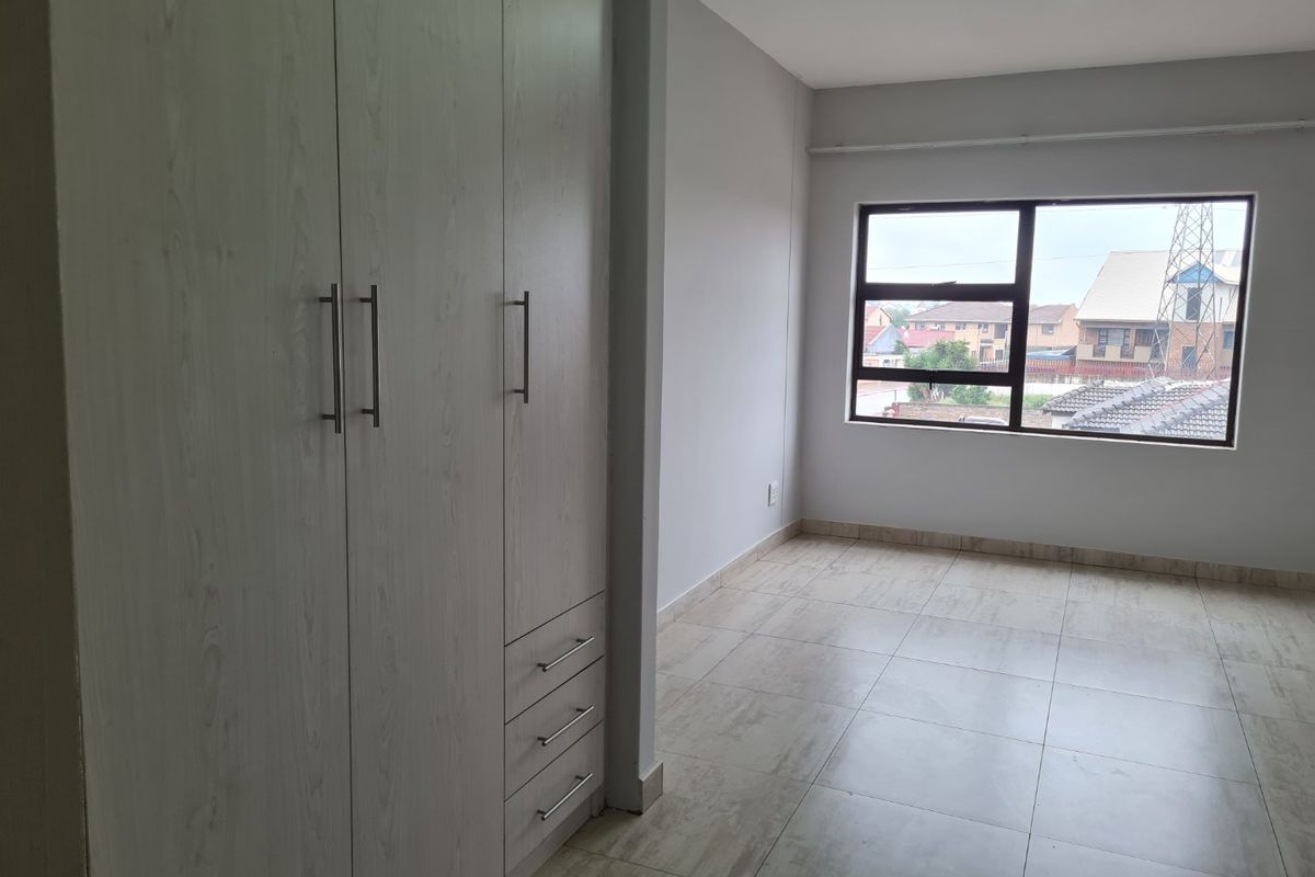 A bright, empty bedroom featuring neutral tiled flooring and modern built-in cupboards with light wood-grain finish.