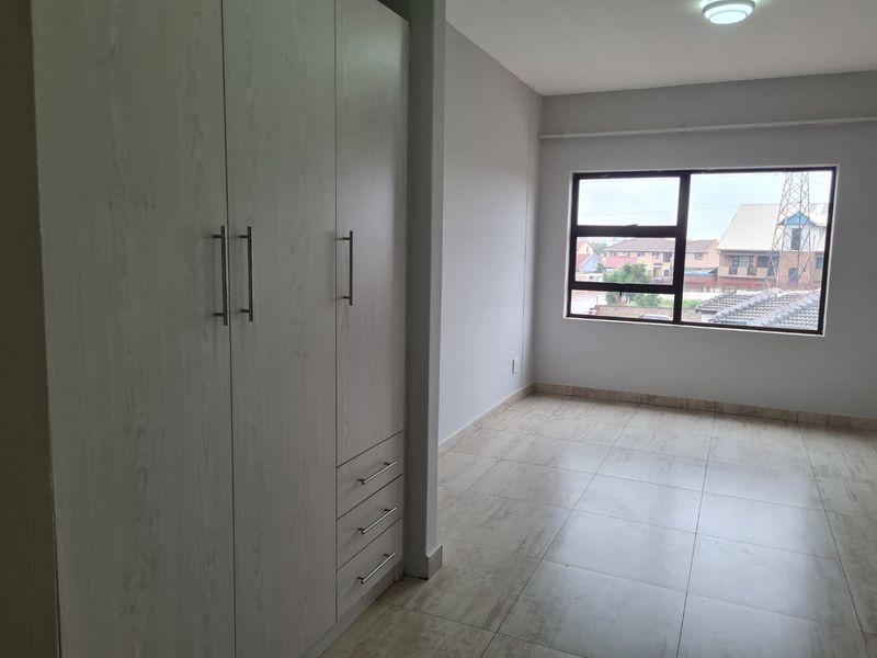A bright, empty bedroom featuring neutral tiled flooring and modern built-in cupboards with light wood-grain finish.