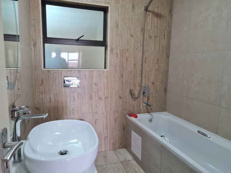 Modern bathroom featuring a vessel sink, chrome fixtures, and a bathtub with wood-look tiled wall accents.