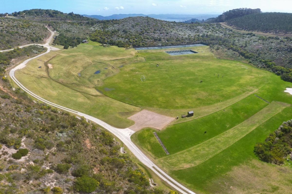 Aerial view of a large, open residential land parcel featuring a cleared grass field, gravel access road, and a small pond.