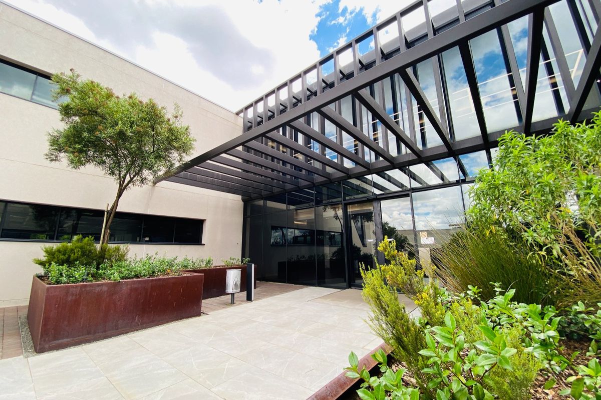 Modern commercial building entrance featuring a striking metal pergola, glass facade, and contemporary corten steel planters in a well-maintained landscaped setting.