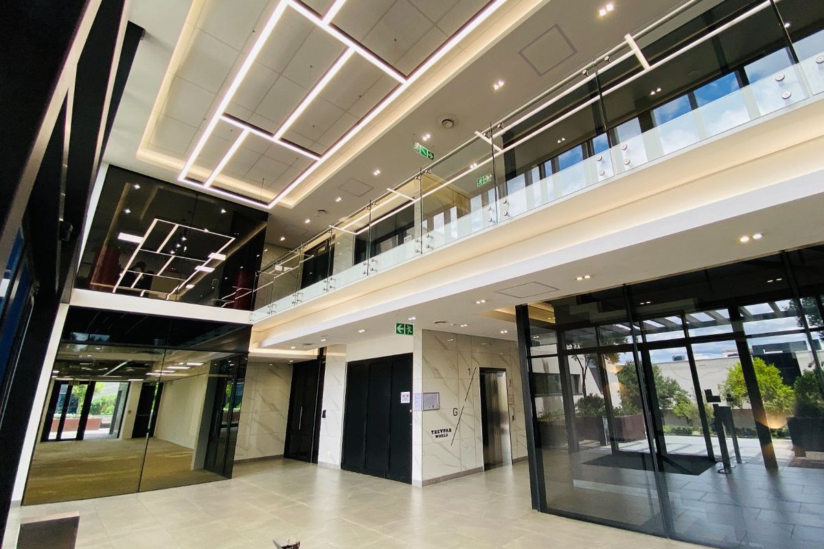 Modern double-volume commercial lobby featuring high-end finishes, glass balustrades, integrated LED lighting, and a sleek elevator access point.