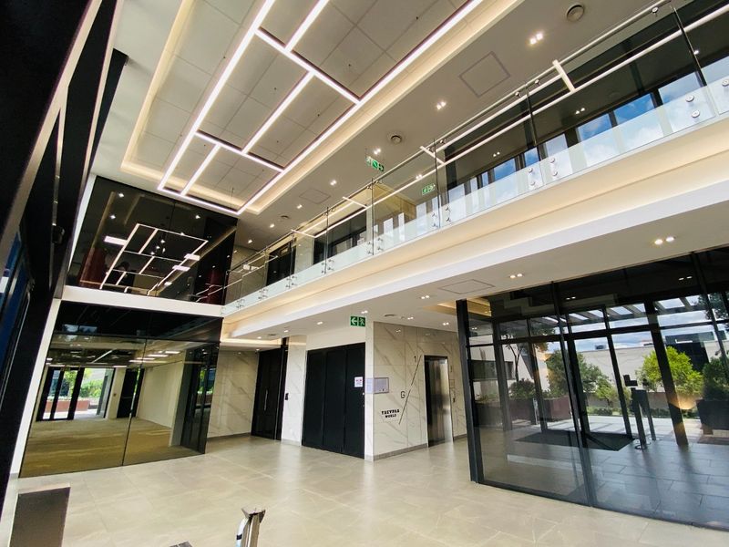 Modern double-volume commercial lobby featuring high-end finishes, glass balustrades, integrated LED lighting, and a sleek elevator access point.