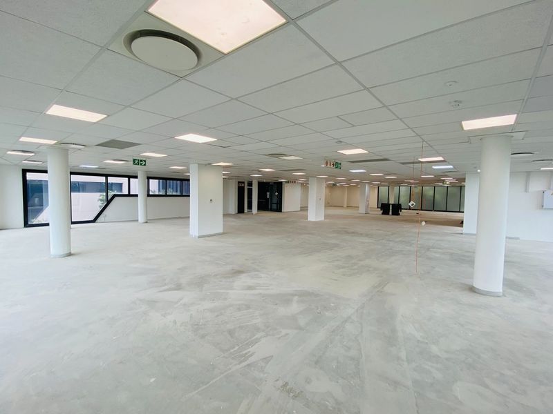 A large, open-plan commercial office space featuring a suspended ceiling, recessed lighting, and structural columns, currently awaiting final flooring installation.