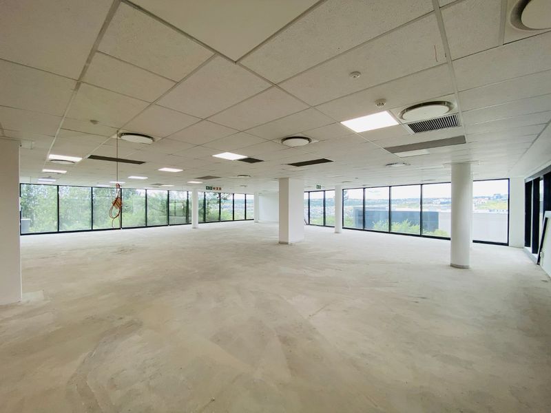 Spacious open-plan commercial office area featuring floor-to-ceiling windows, suspended ceilings, and structural columns, currently in a shell condition ready for fit-out.