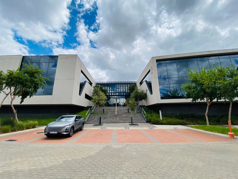 Modern commercial office building featuring a striking glass facade, concrete structure, and a central staircase leading to the main entrance.