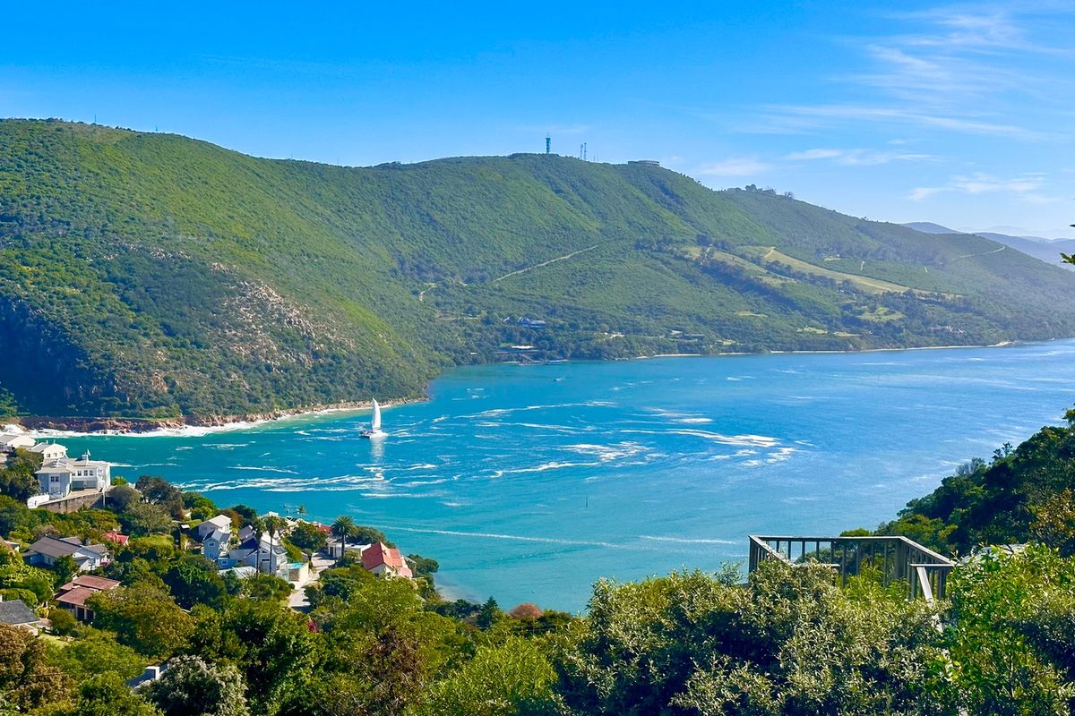 A scenic elevated view overlooking the bay, coastline, and surrounding hills, featuring a wooden viewing deck in the foreground.