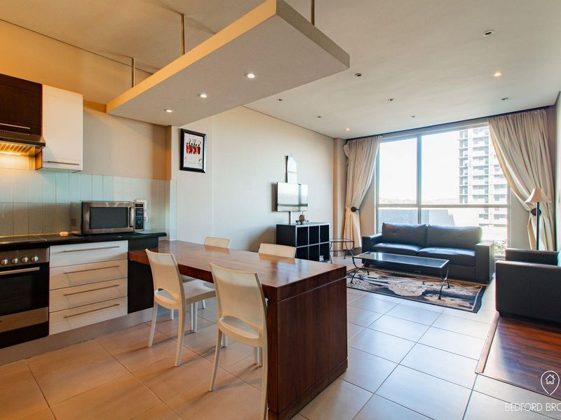 Modern open-plan apartment featuring a sleek kitchen with built-in appliances, tiled flooring, and expansive windows offering natural light and urban views.