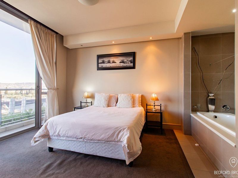 Spacious bedroom featuring an integrated bathtub, recessed lighting, and a large sliding glass door opening onto a private balcony with scenic views.