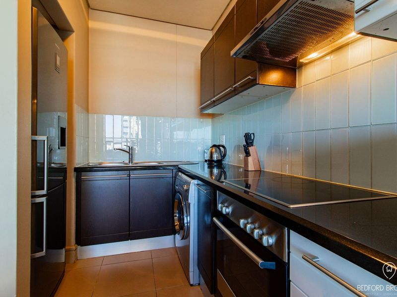 Modern galley-style kitchen featuring dark cabinetry, black stone countertops, integrated appliances, and a sleek tiled backsplash.