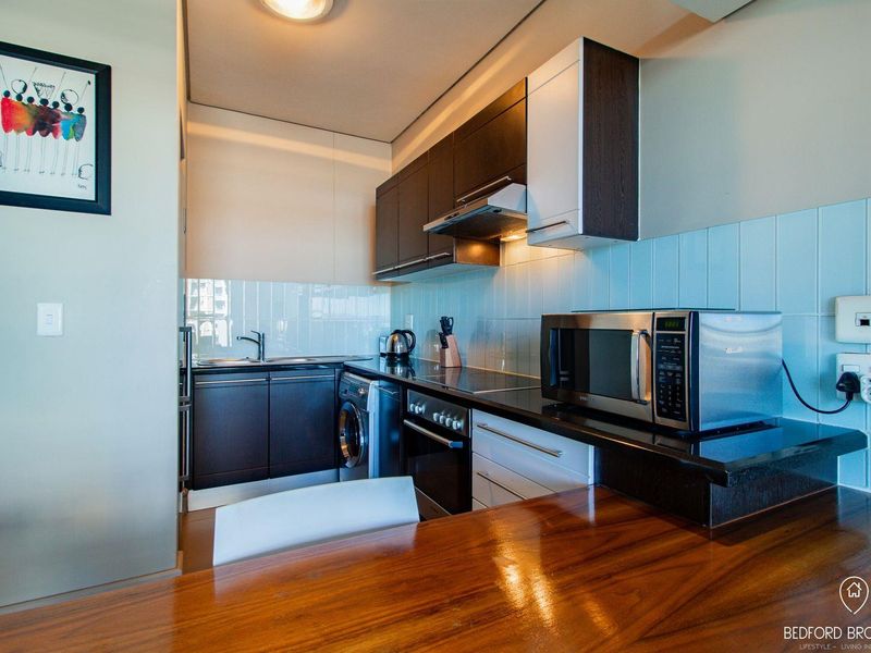 Compact modern kitchen featuring dark cabinetry, stone countertops, integrated appliances, and a light blue tiled splashback.