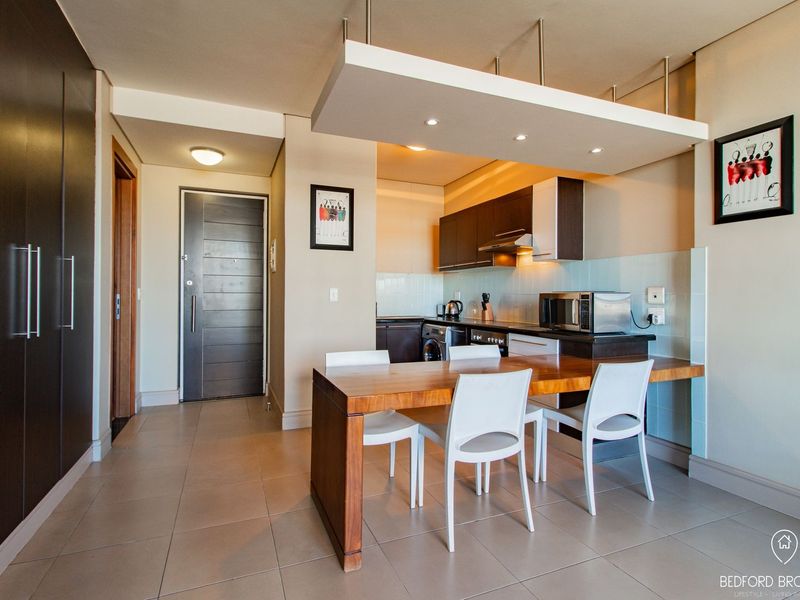 Modern open-plan kitchen and dining area featuring sleek built-in cabinetry, integrated appliances, tiled flooring, and a stylish suspended bulkhead with recessed lighting.