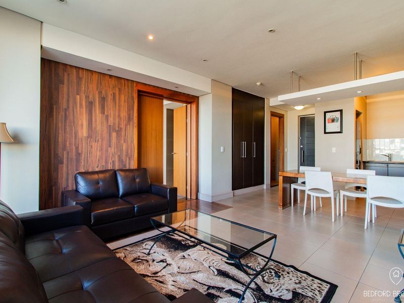 Modern open-plan living and dining area featuring tiled floors, wood paneling accents, and a sleek integrated kitchen with contemporary cabinetry.