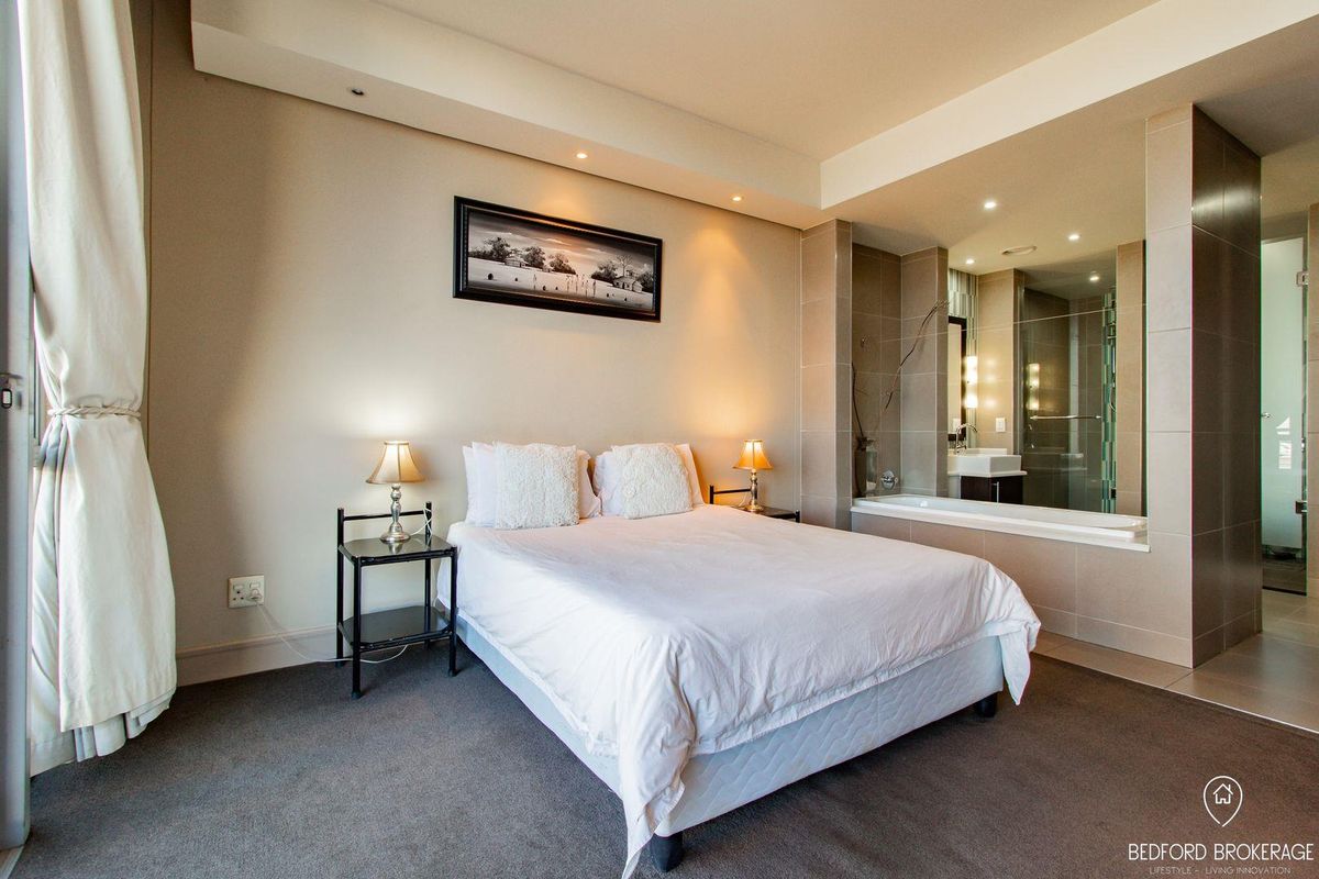 Spacious bedroom featuring an open-plan en-suite bathroom with a built-in bathtub, glass shower, and modern vanity, complemented by neutral finishes and recessed lighting.