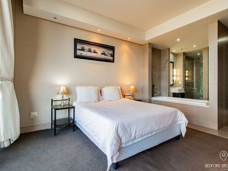 Spacious bedroom featuring an open-plan en-suite bathroom with a built-in bathtub, glass shower, and modern vanity, complemented by neutral finishes and recessed lighting.