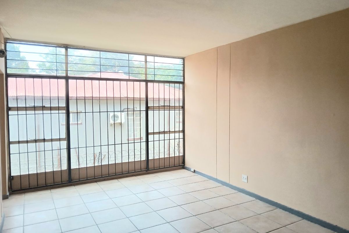 An empty living room featuring tiled flooring and large windows with security bars, offering a blank canvas for interior design.