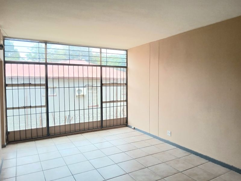 An empty living room featuring tiled flooring and large windows with security bars, offering a blank canvas for interior design.
