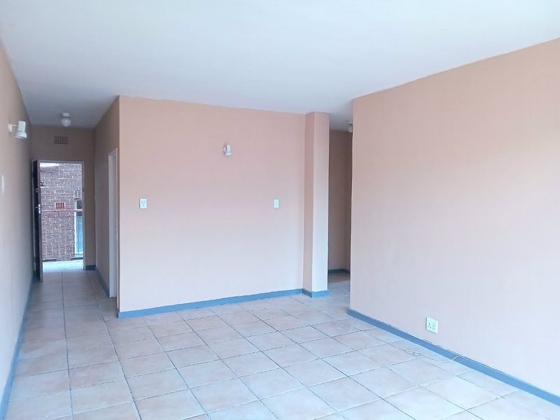An empty, open-plan living area featuring neutral-toned walls, ceramic tiled flooring, and simple wall-mounted lighting fixtures.