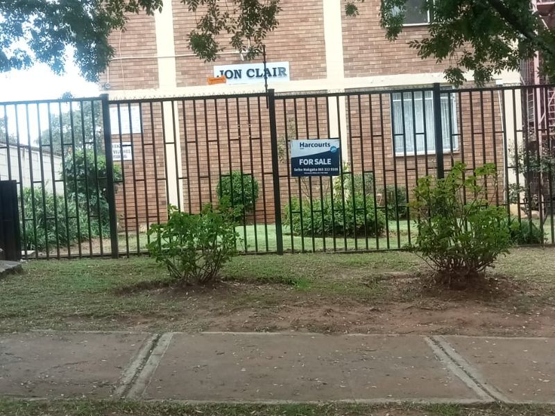 Front view of the Jon Clair apartment building featuring a brick facade and secure perimeter fencing.
