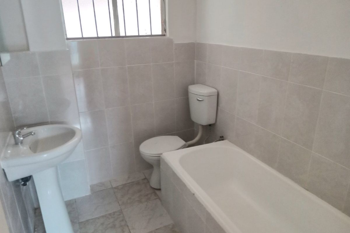 A functional bathroom featuring a pedestal basin, toilet, and bathtub with neutral wall and floor tiling.