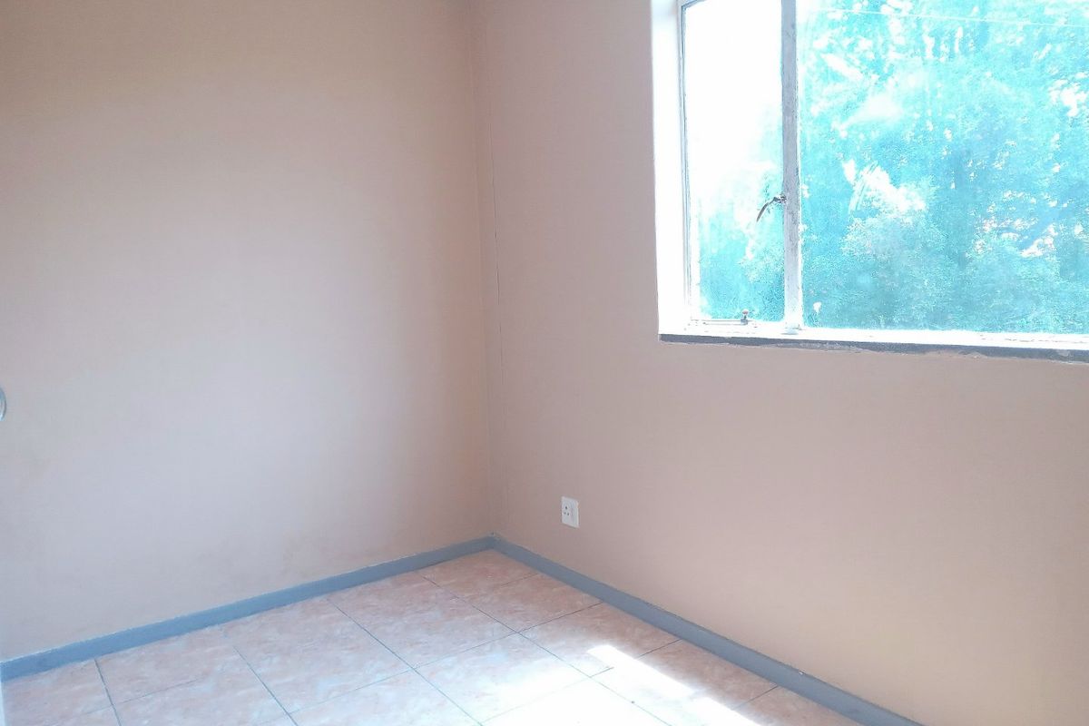 An empty bedroom featuring tiled flooring, neutral wall paint, and a large window providing natural light.