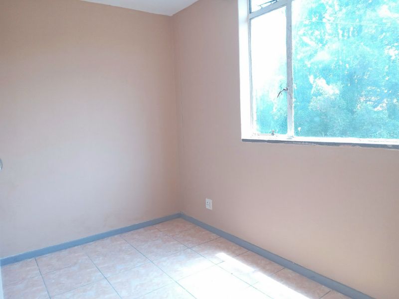 An empty bedroom featuring tiled flooring, neutral wall paint, and a large window providing natural light.