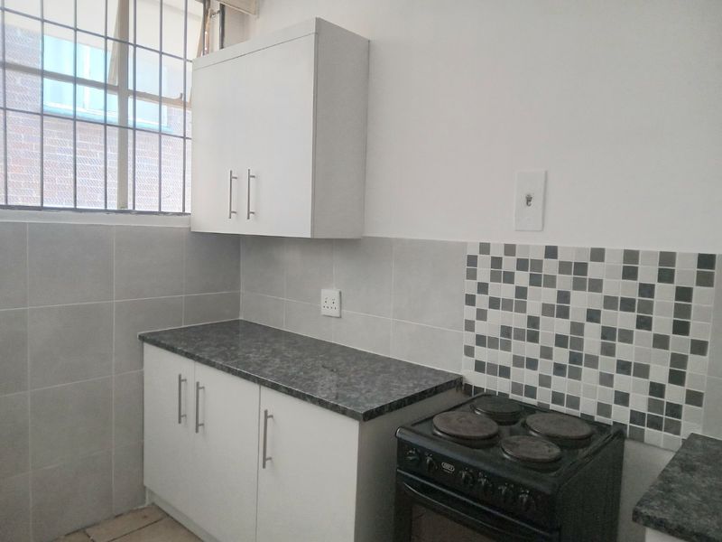 A functional kitchen area featuring white cabinetry, grey tiled splashbacks, a laminate countertop, and a freestanding electric stove.