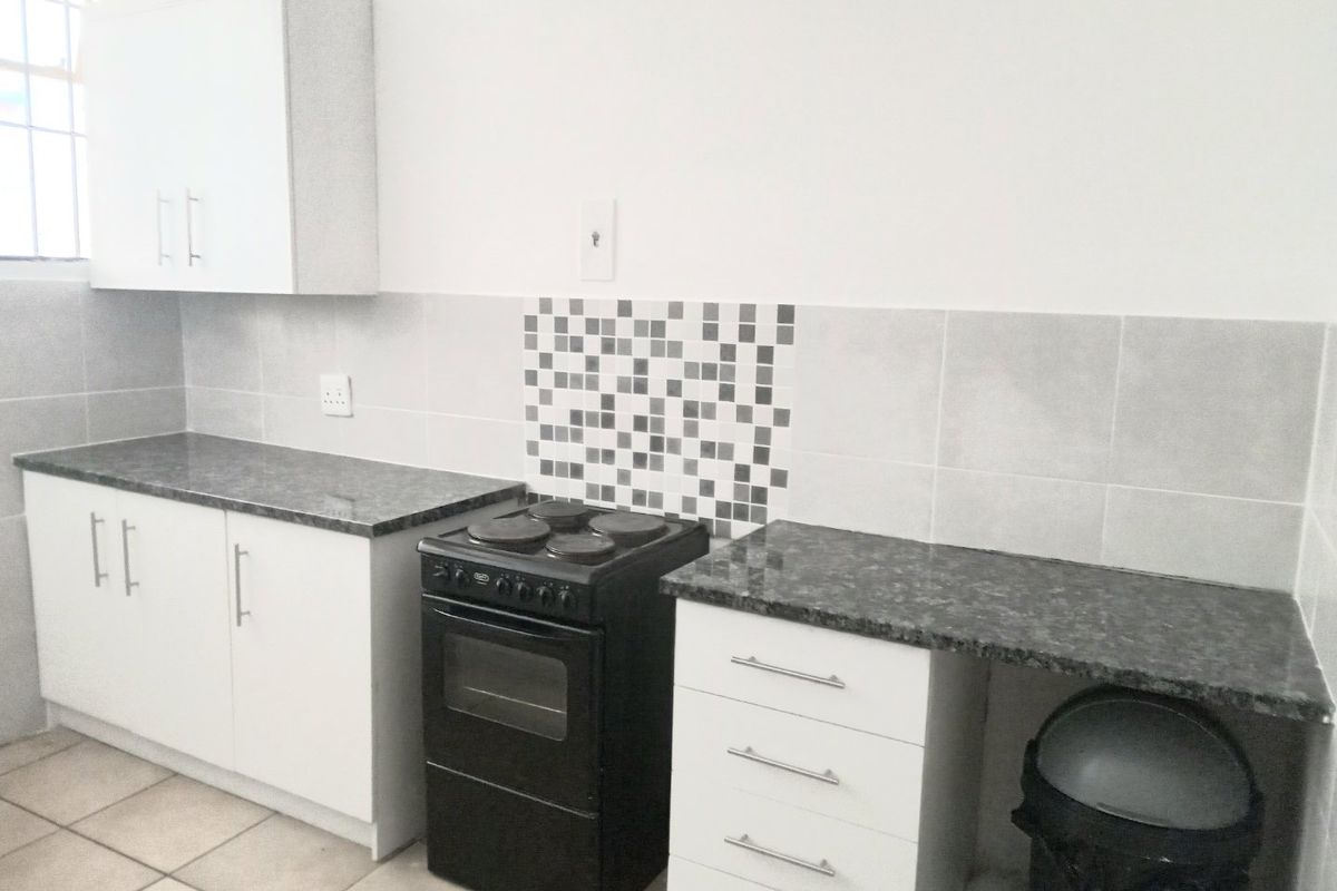 A functional kitchen featuring white cabinetry, granite-look countertops, a tiled backsplash, and a freestanding electric stove with oven.
