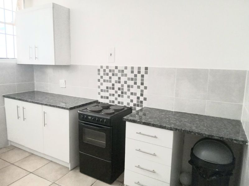 A functional kitchen featuring white cabinetry, granite-look countertops, a tiled backsplash, and a freestanding electric stove with oven.