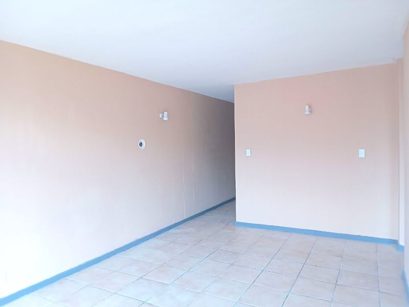 An empty, open-plan living area featuring neutral-toned walls, tiled flooring, and wall-mounted lighting fixtures, providing a blank canvas for interior design.