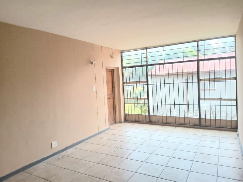 An empty living area featuring tiled flooring, a wooden door, and large windows secured with metal burglar bars.