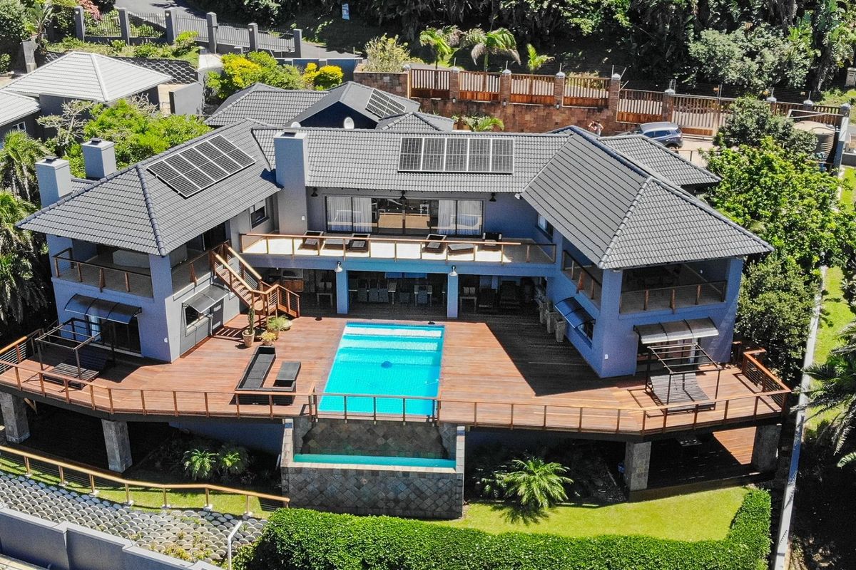 Aerial view of a modern multi-level residence featuring extensive timber decking, a swimming pool, and solar panels on a tiled roof.